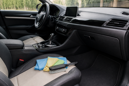 Car interior showing leather seats, textured plastic trim, fabric upholstery, glass windows, and a central touchscreen prepared for surface-specific cleaning