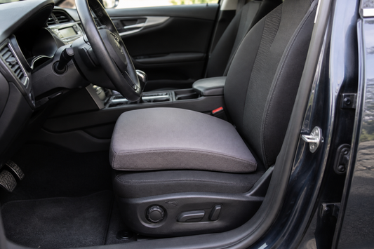 Neutral car seat cushion centered on the driver seat with the steering wheel and pedals visible
